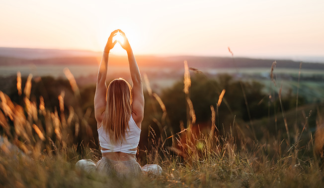 Frau mit Yogapose vor Sonnenaufgang